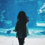 small child touching aquarium glass with fish