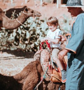 kid riding on brown camel beside man wearing green coat at daytime