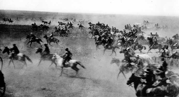 black and white photo of the Oklahoma Land Rush in 1889 of many people running their horses with dirt stirring up