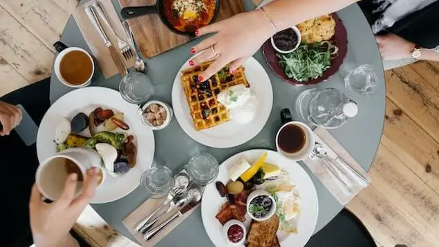 table with plats of breakfast food such as waffles, bacon, eggs, and toast