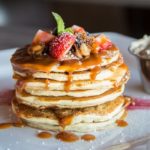 stack of pancakes with strawberries, nuts, and caramel on top