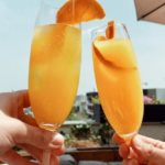 2 people cheering with 2 glasses of mimosas