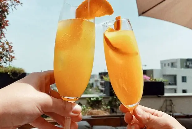 2 people cheering with 2 glasses of mimosas