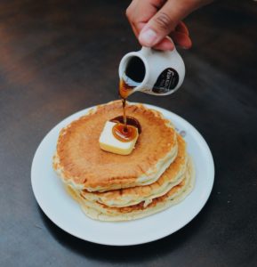 pancakes with butter and someone pouring syrup on top