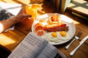 plate of eggs, bacon, pancakes, oranges with someone holding a glass of orange juice