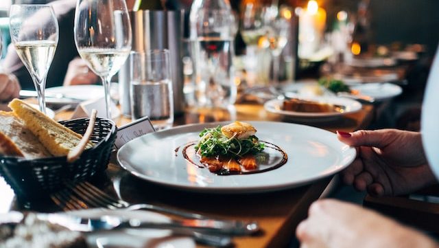 food on a plate with wine glasses and bread beside it on a table