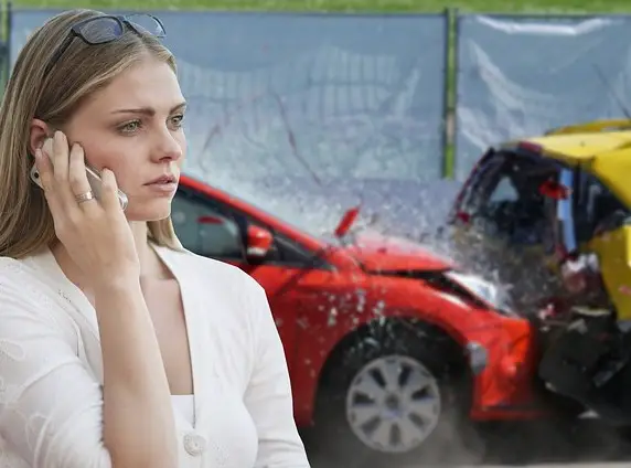 red car rear-ended and smashed a yellow car.  A woman on the foreground is making a call on her cell phone