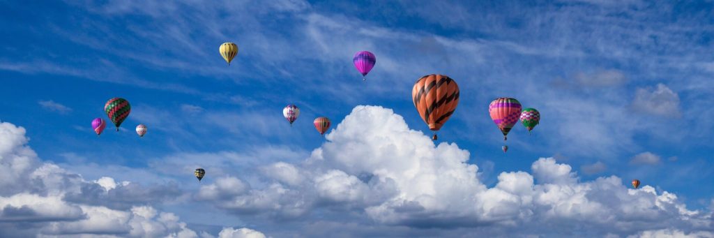 several hot air balloons flying in the sky with clouds in the background