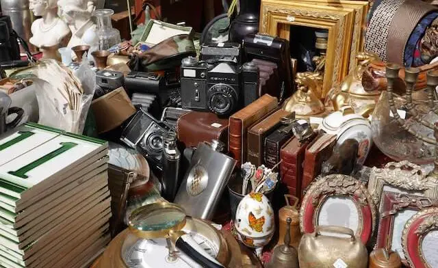 table of flea market goods for sale such as cameras, books, clock, magnifying glass, other miscellaneous items