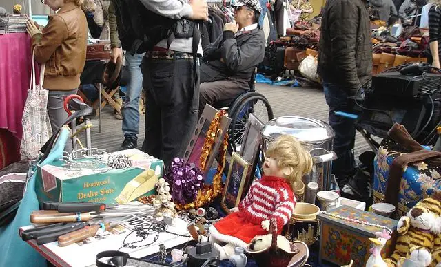 miscellaneous goods sitting on a table at a flea market with people shopping in the background