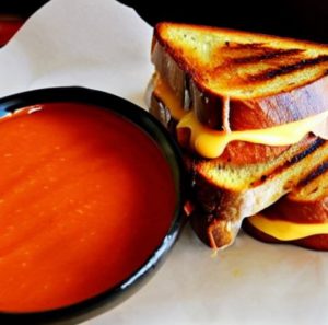 gourmet grilled cheese sandwich next to tomato soup