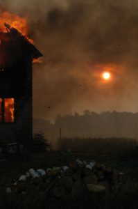 house on fire with sun shining through smoke