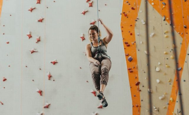woman hanging from a rope beside a rock climbing wall