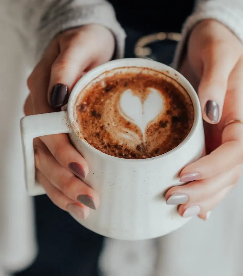 person holding white ceramic mug with brown liquid