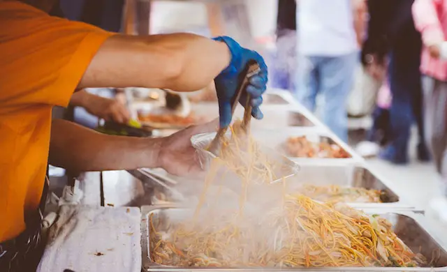 employee serving noodles in to-go container