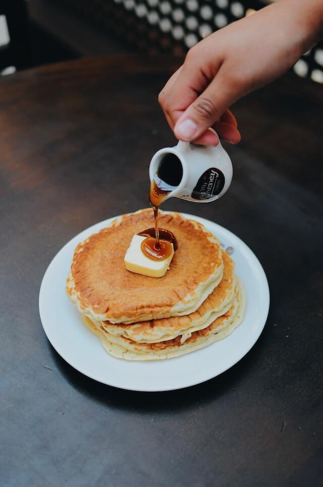 hand pouring syrup on top of pancakes and butter