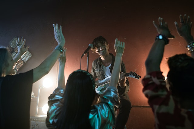 man playing guitar on a stage with people dancing in the foreground