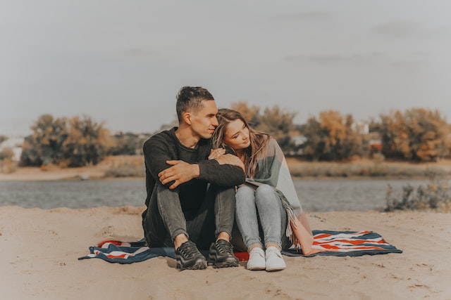 man and woman sitting in the sand by the lake