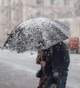 person standing by a street holding an umbrella while it's snowing