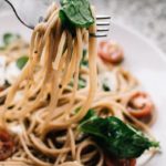 Italian food on a plate with noodles, tomatoes, and basil