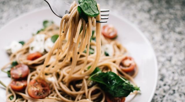 Italian food on a plate with noodles, tomatoes, and basil