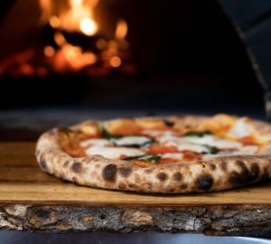 wood fired pizza sitting on a board with a wood fire oven in the background