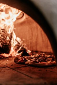 pizza being cooked by wood burning oven