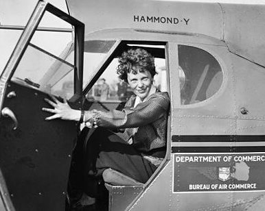 Amelia Earhart sitting in a grounded airplane with the door open