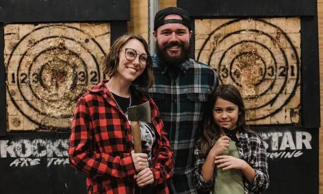 woman, man, and child standing in front of axe throwing target
