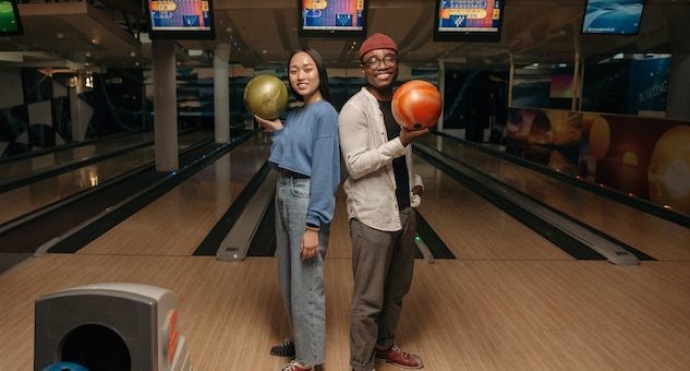 woman and man each holding a bowling ball with the bowling lanes behind them