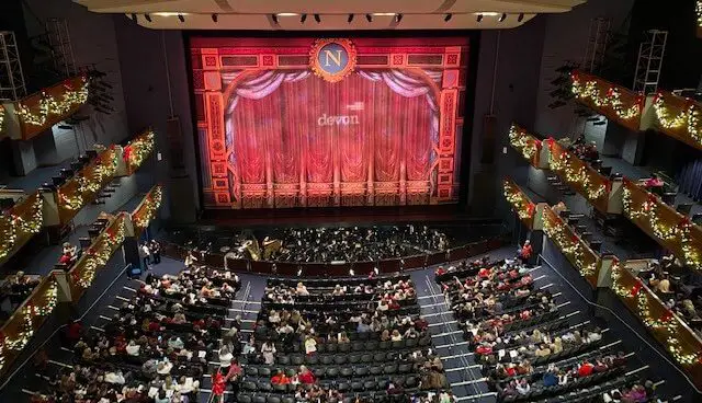 large music hall with large screen and curtains and lots of people