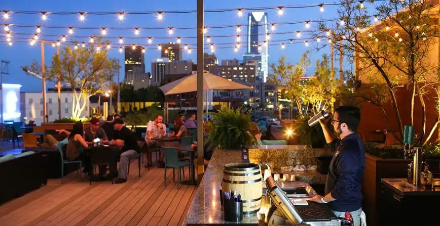 people having dinner and drinks on a rooftop with oklahoma city skyline in the background