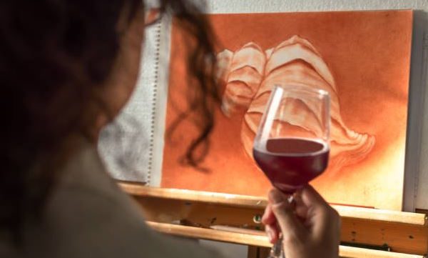 woman holding wine looking at a painting on canvas