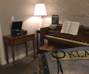 a rom with a piano, lamp, record player, and a blanket that says Oklahoma