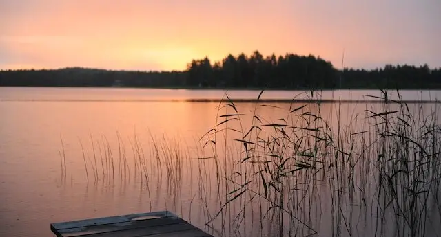 lake with a dock in the foreground and trees and sunset in the background