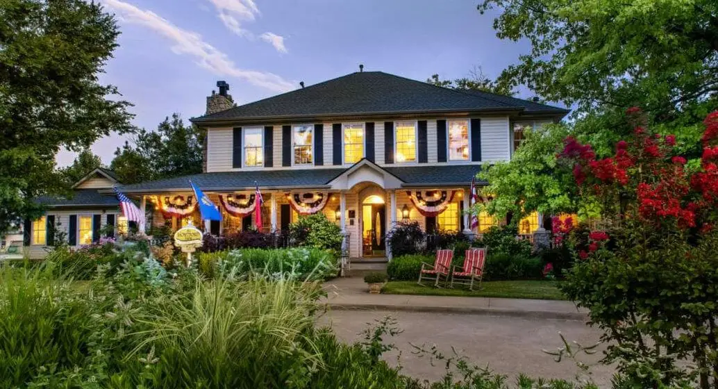 front of a white two story house with lots of pretty green shrubbery and treets