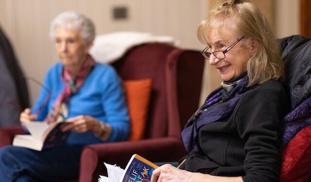 2 older women sitting in a chair with a book