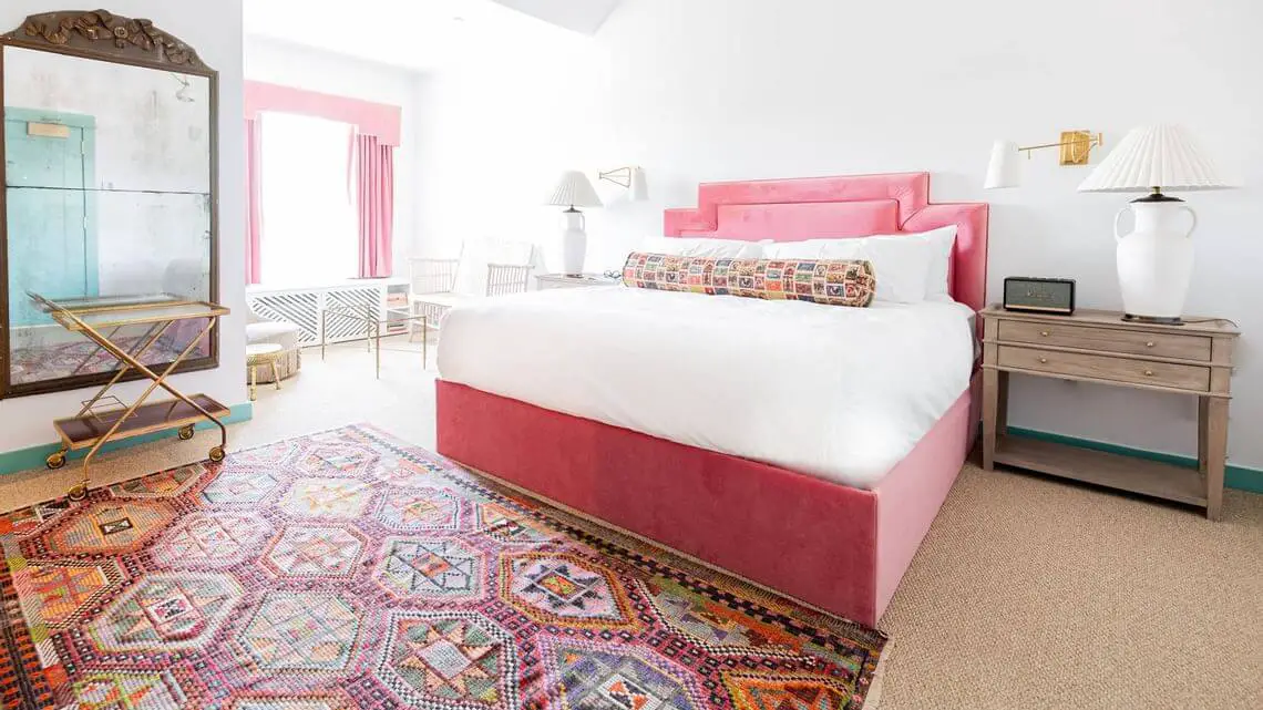 hotel room with pink bed, area rug, pink curtains, large mirror