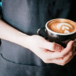 person holding a cup of coffee with latte art