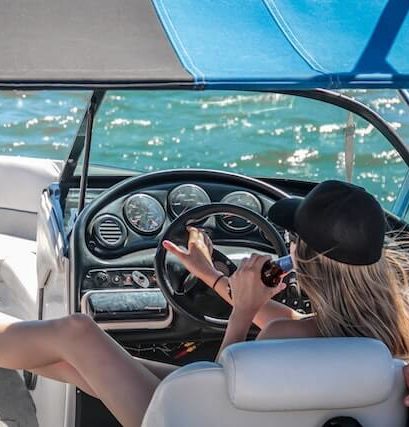 woman sitting behind steering wheel of boat drinking a beverage