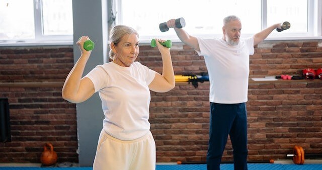 a senior man and woman lifting barbells 