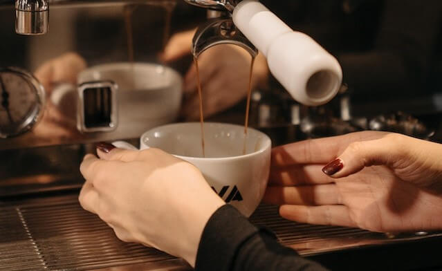 coffee pouring out of espresso machine into a cup someone is holding