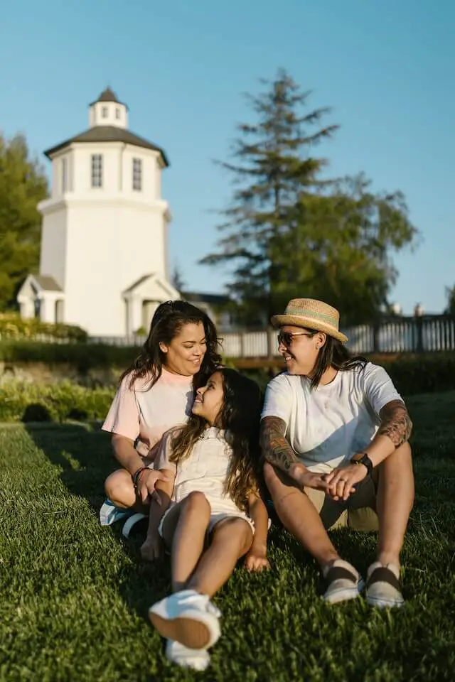 a mom, dad, and daughter sitting on a grassy lawn