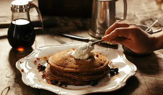 a hand spreading whipped butter on a plate of pancakes