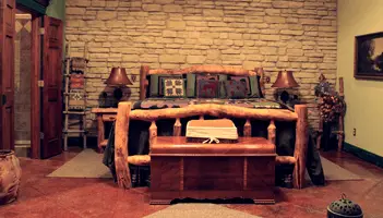 rustic bedroom set with bed made of timber, wooden chest, and rock wall behind it