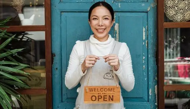 woman holding open sign in front of a door