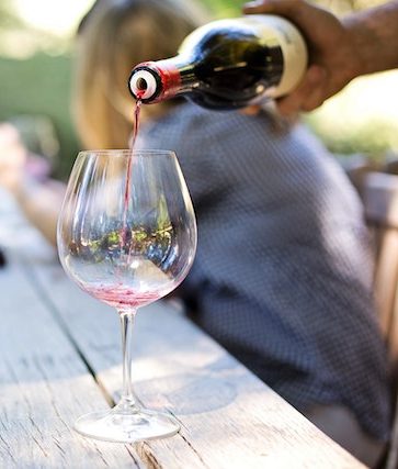 bottle of wine being poured into a glass sitting on a wooden table