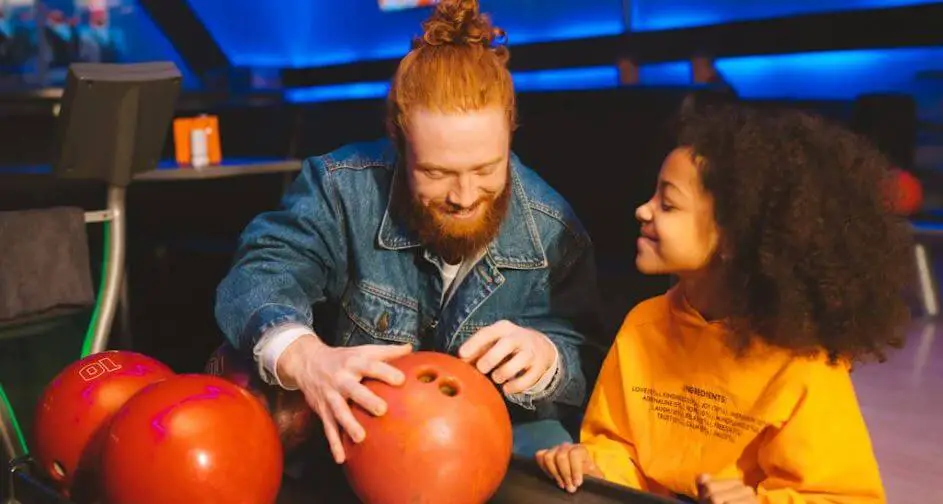 man showing small girl a bowling ball