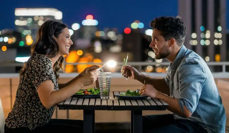 man and woman eating on a rooftop with city lights in the background
