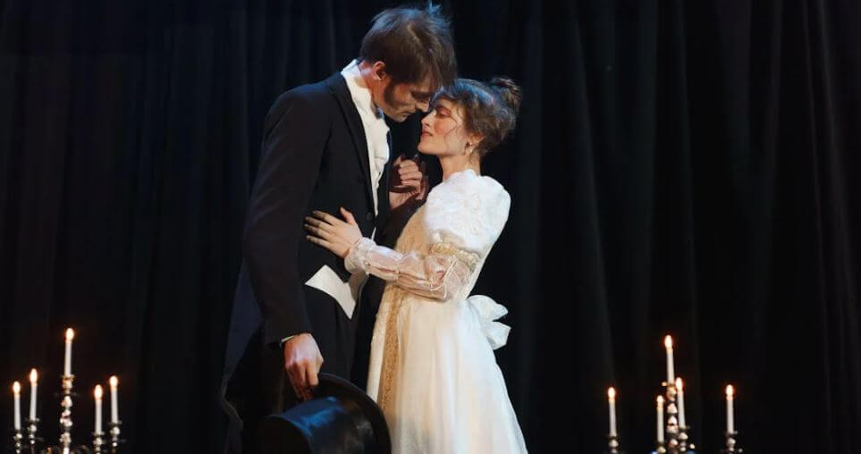 man on woman on stage with candles during a play about to kiss